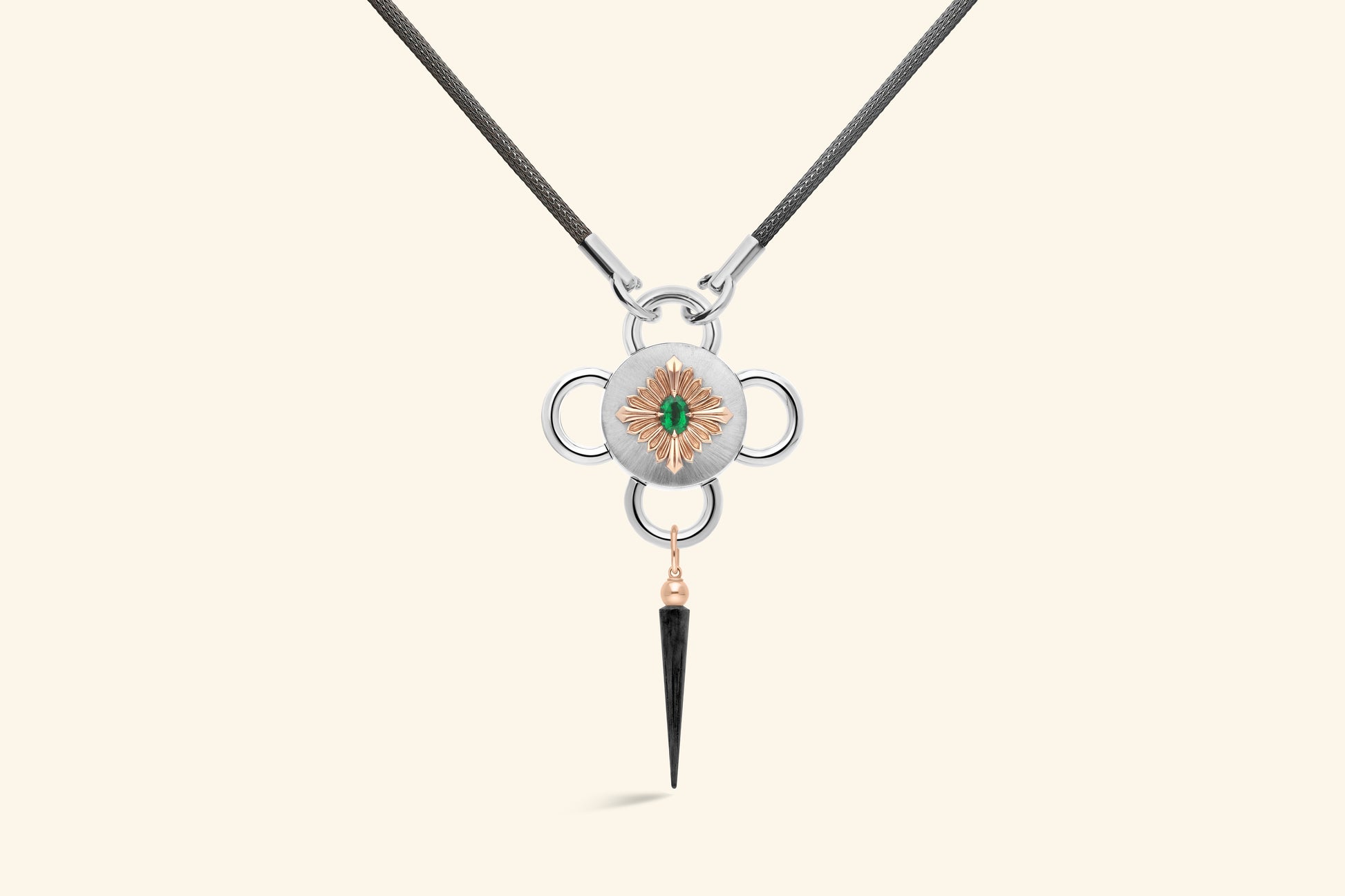 Collier Bolt, émeraude de ~0,80 carat sertie une fleur en or rose poli, elle-même posée sur un plateau en argent satiné. Une pampille en or rose et argent noirci. Chaine tricotée en argent noirci.